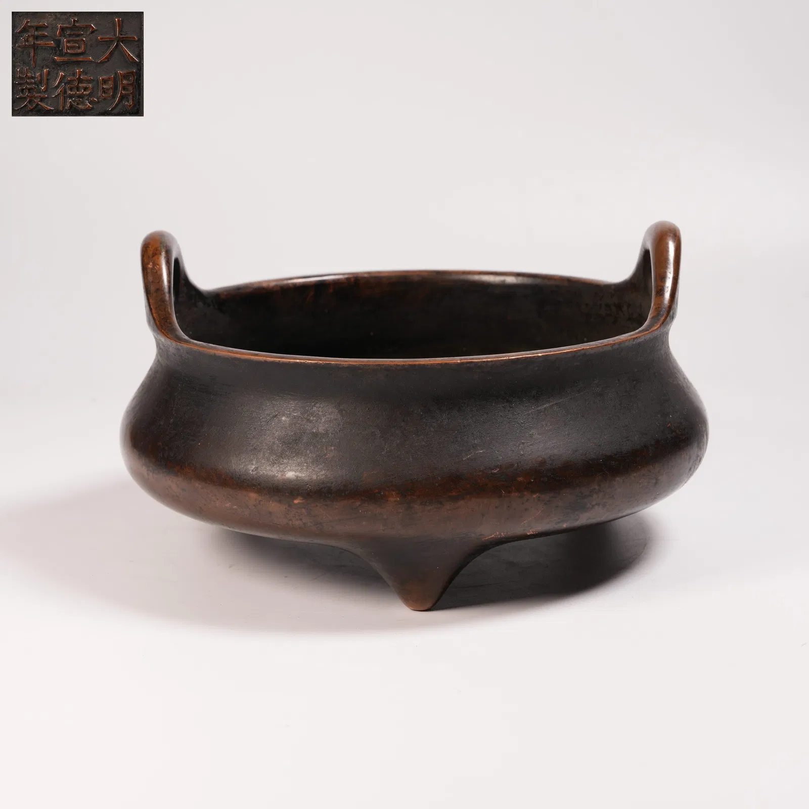 A BRONZE THREE-LEGGED CENSER WITH UPTURNED HANDLES