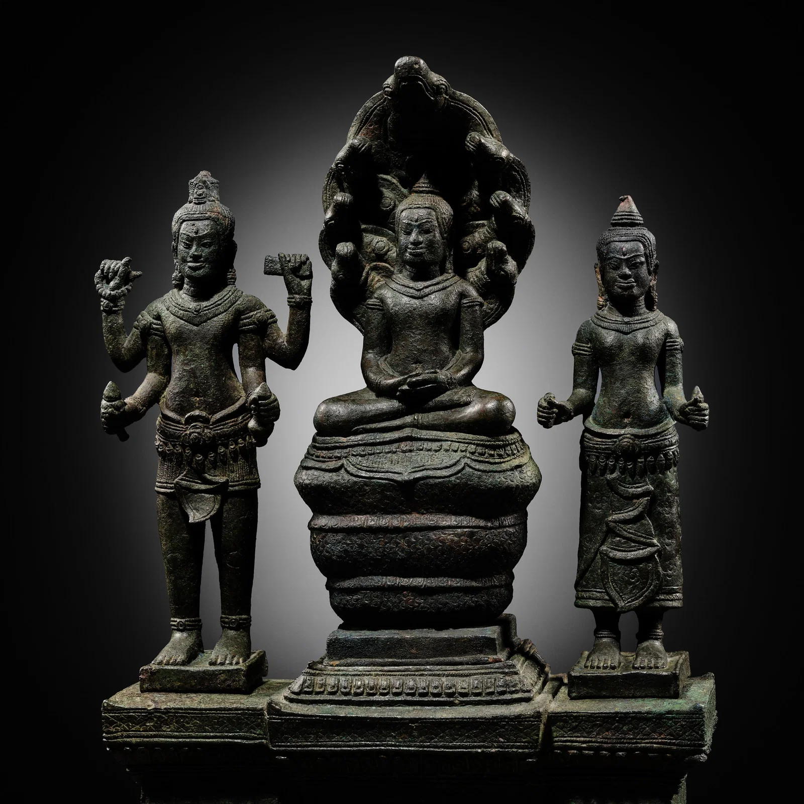 A BUDDHIST BRONZE TRIAD OF BUDDHA MUCHALINDA WITH HIS CONSORTS LOKESHVARA AND PRAJNAPARAMITA, BAYON