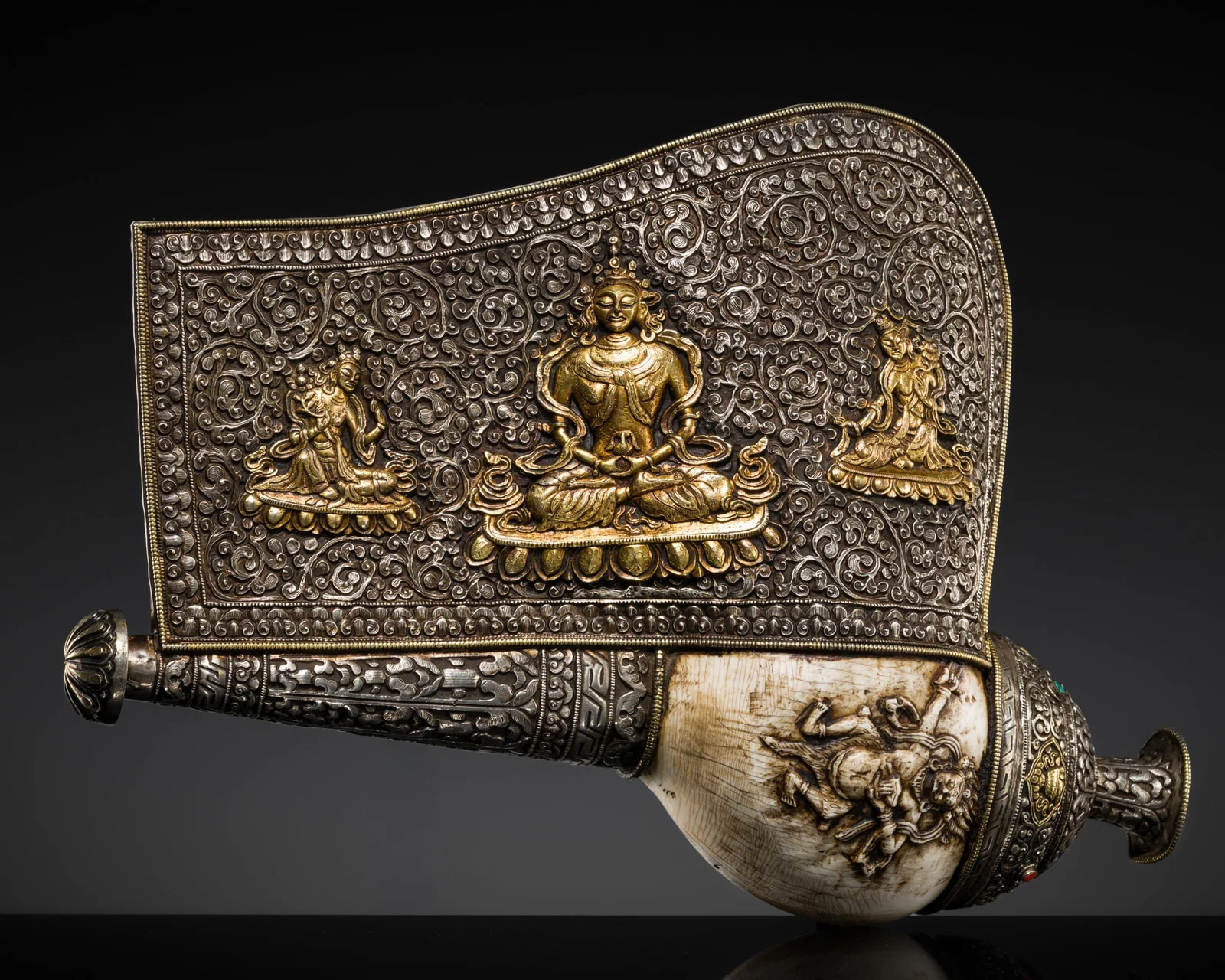 A CARVED CONCH-SHELL TRUMPET, DUNG DKAR, WITH A PARCEL-GILT SILVER REPOUSSÉ MOUNT DEPICTING