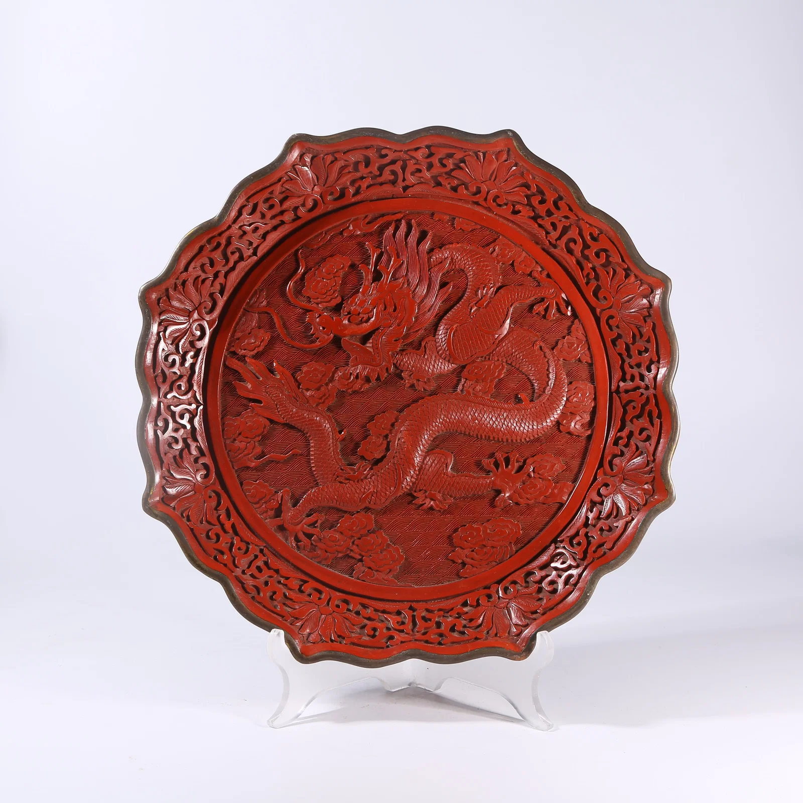 A CARVED RED LACQUER PLATE WITH CLOUD AND DRAGON MOTIF AND FLOWER RIM