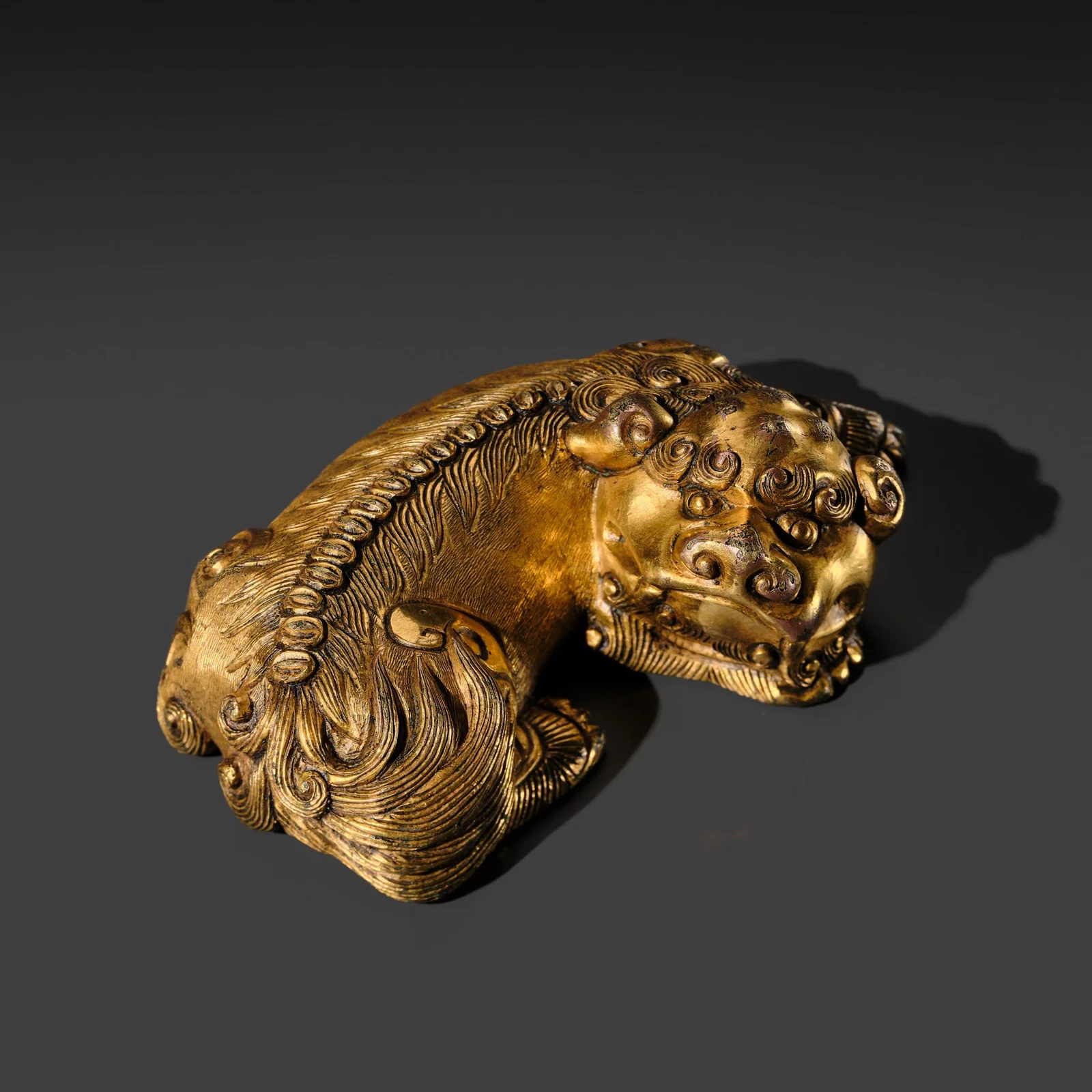 A GILT-BRONZE 'RECUMBENT LION' PAPERWEIGHT, XUANDE MARK AND PERIOD (1425-1435)