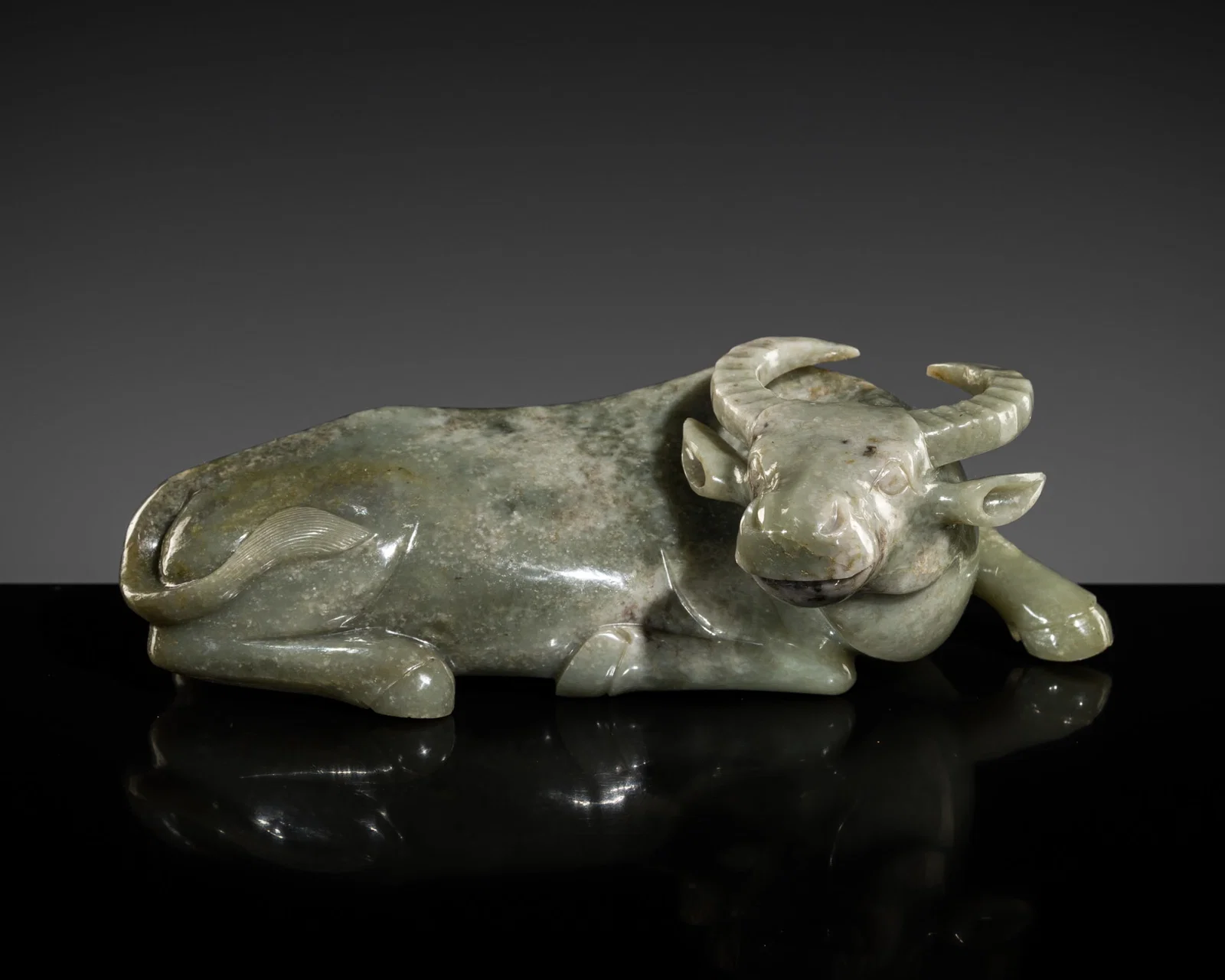 A GRAYISH-GREEN JADE FIGURE OF A WATER BUFFALO, LATE QING DYNASTY-REPUBLIC PERIOD