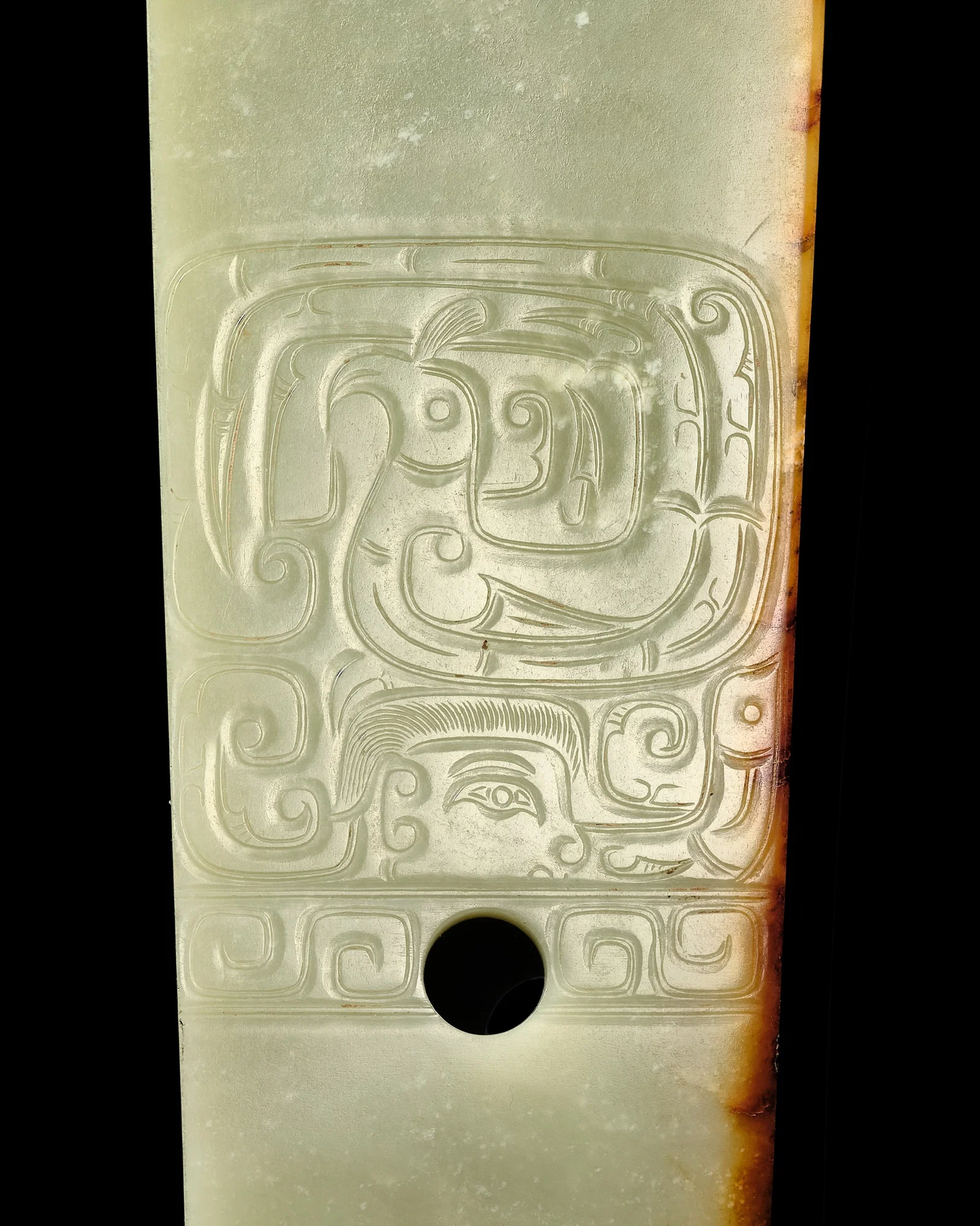A GREEN AND RUSSET JADE 'HUMAN AND BIRD' CEREMONIAL BLADE, WESTERN ZHOU DYNASTY