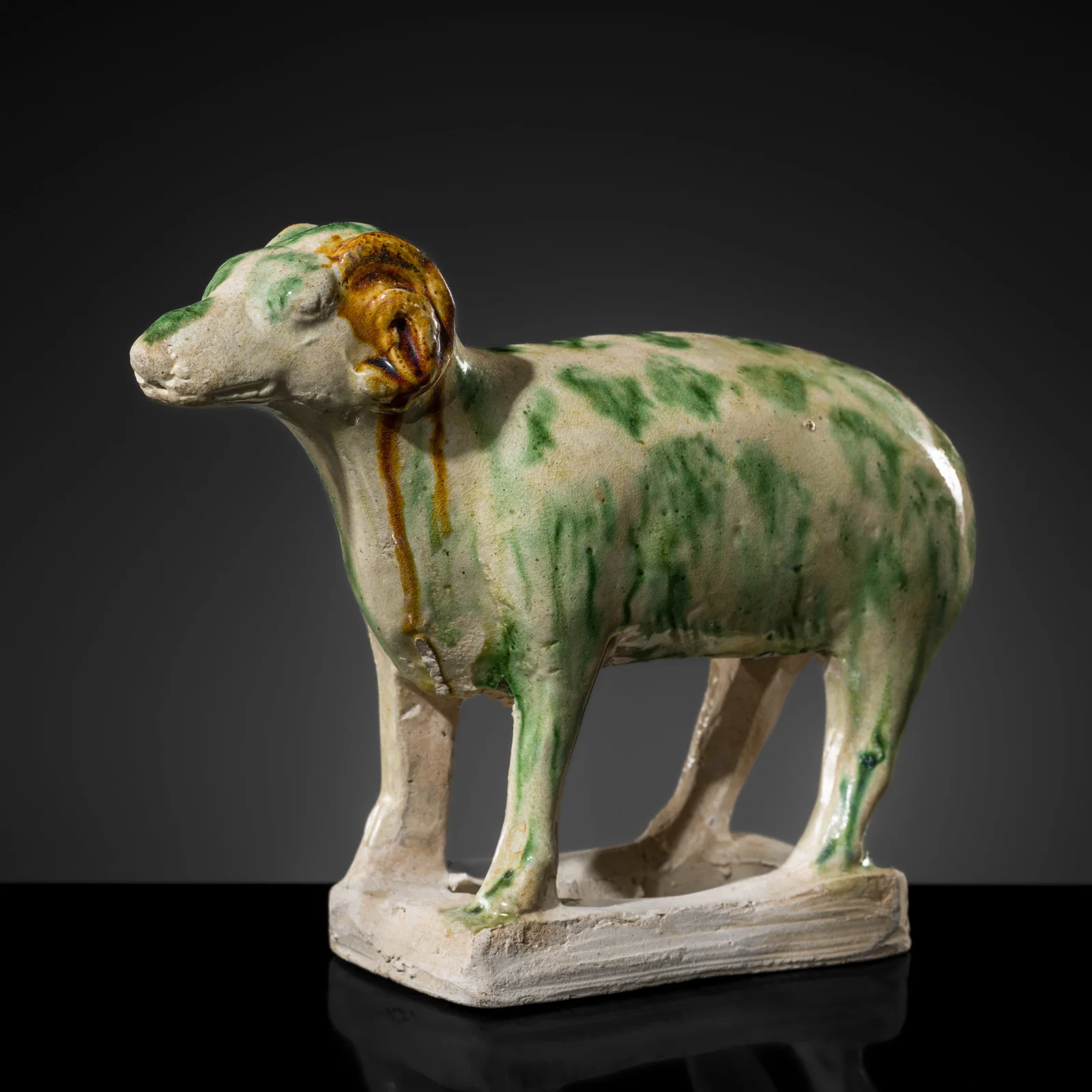 A RARE SANCAI SPLASHED POTTERY FIGURE OF A RAM, TANG DYNASTY