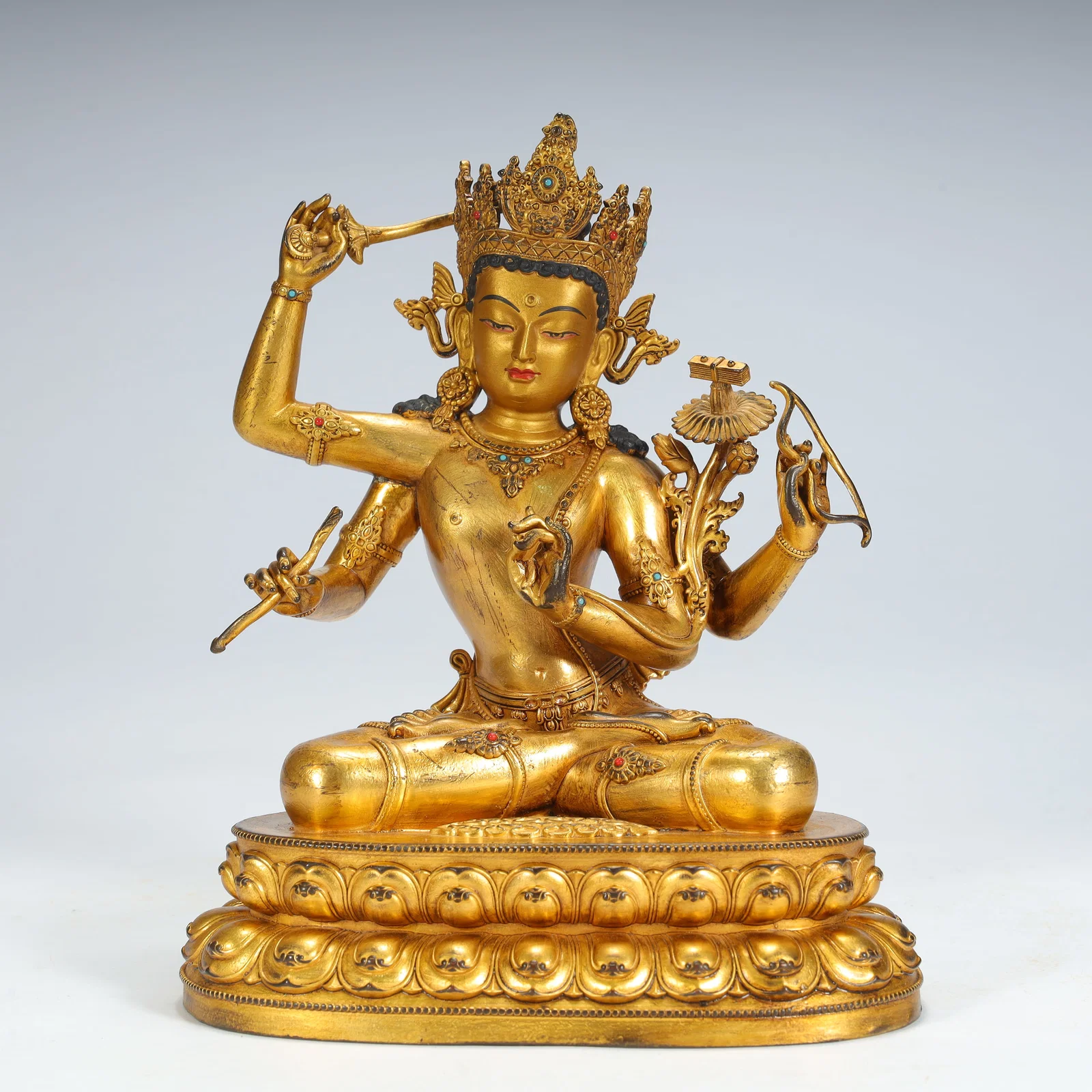 A seated statue of Manjushri Bodhisattva with four arms in copper gilt inlaid treasures in the Qing