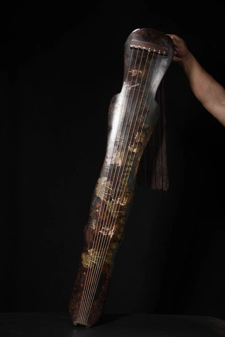 A seven-stringed guqin with a wooden base, lacquered and decorated with a gold-painted image of the