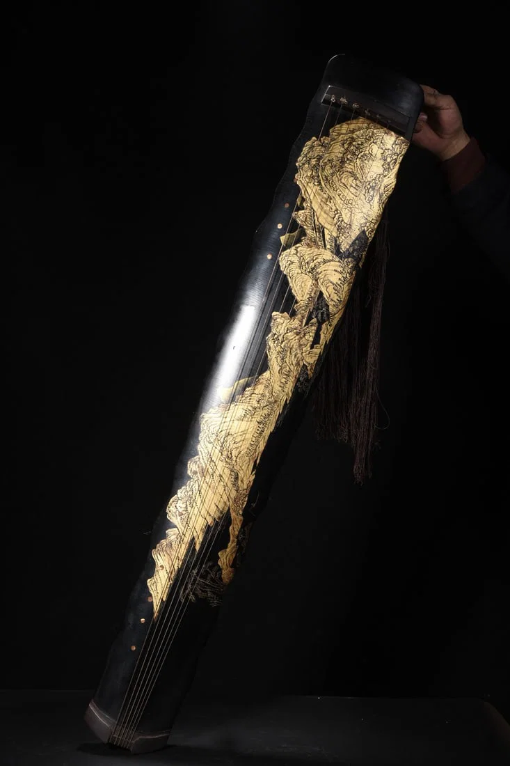 A seven-stringed guqin with a wooden base, lacquered and decorated with a gold-painted landscape