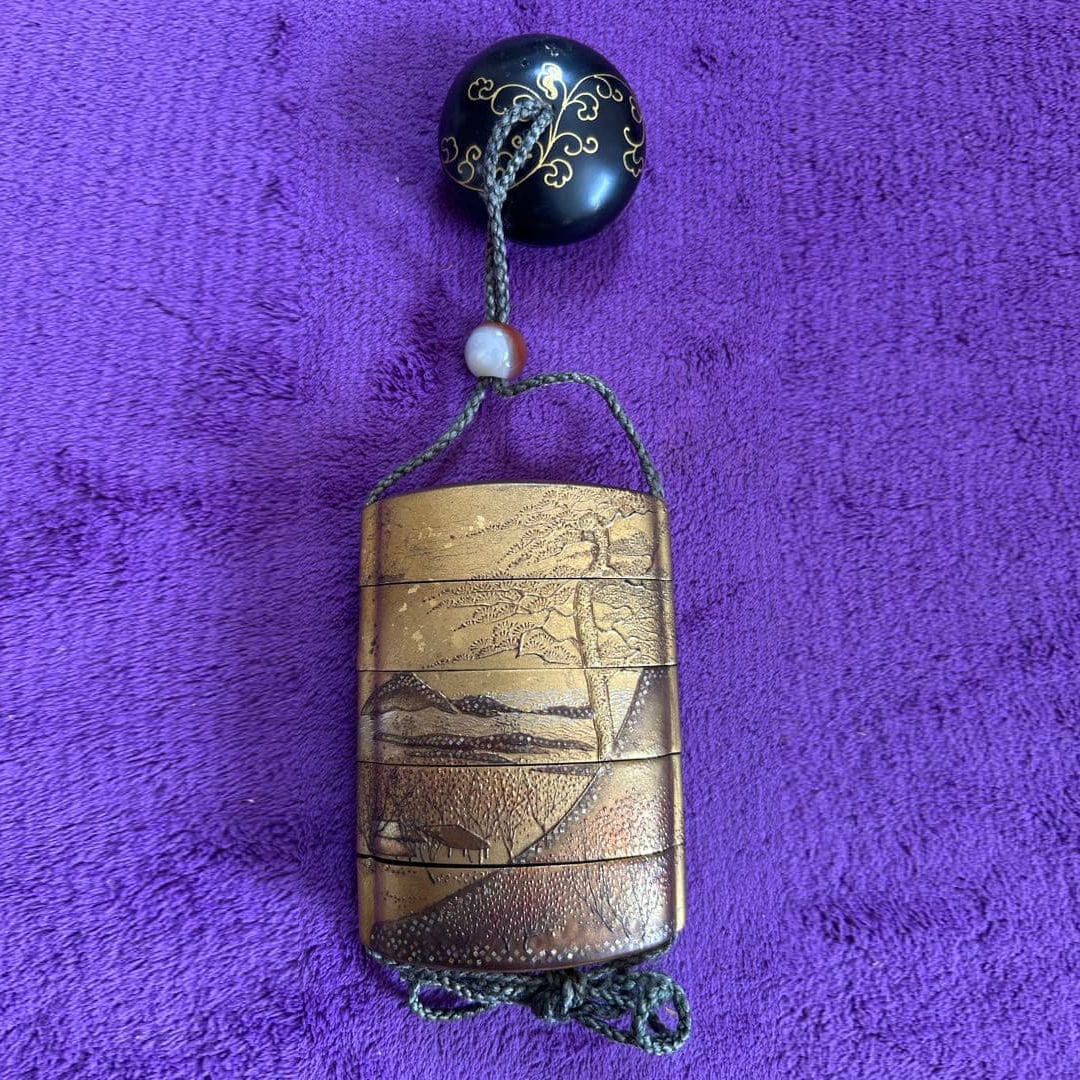 Lacquerware inrO (small container), adorned with a gold leaf landscape netsuke (miniature carving).